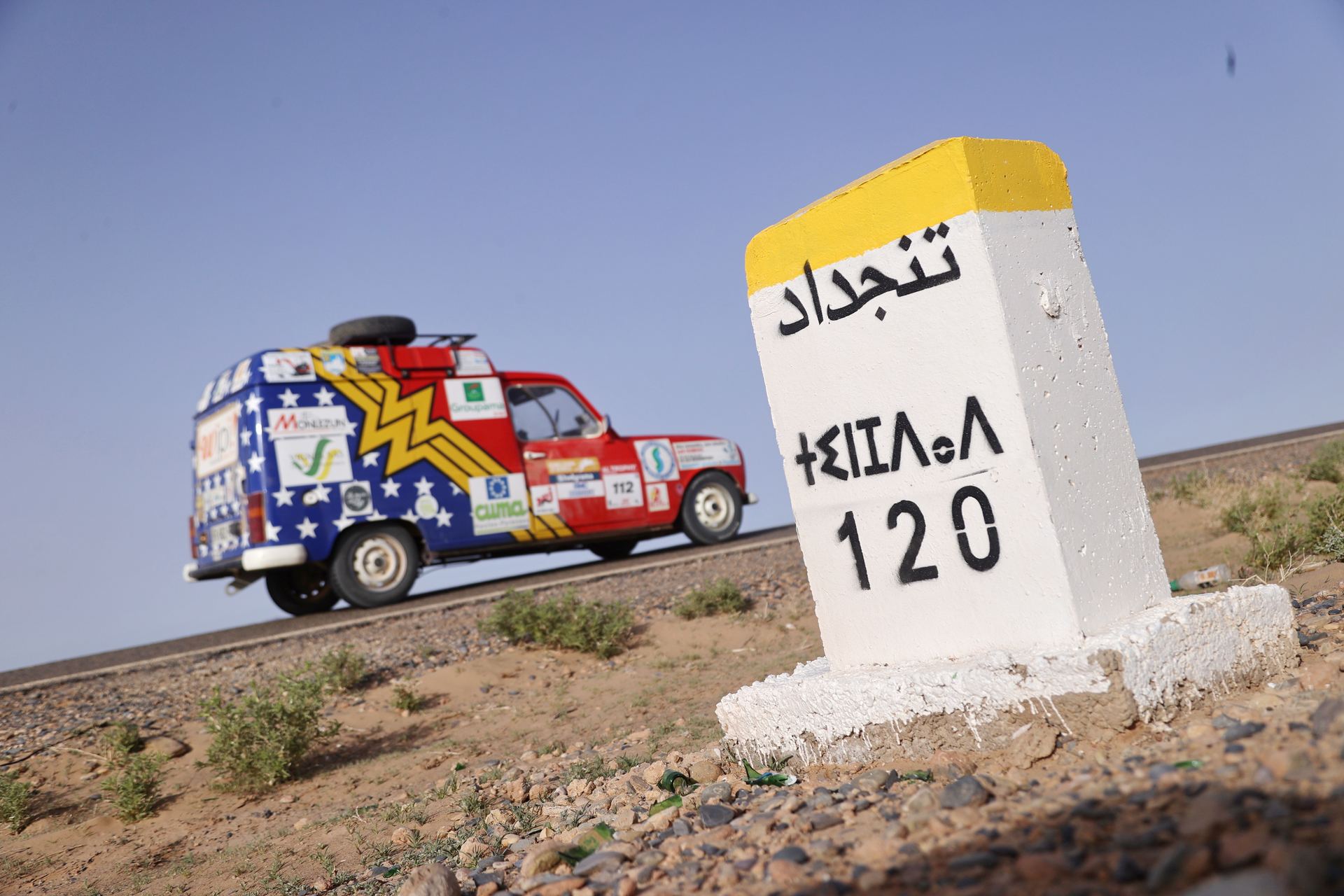 Une 4L du raid devant une borne kilométrique dans le désert marocain